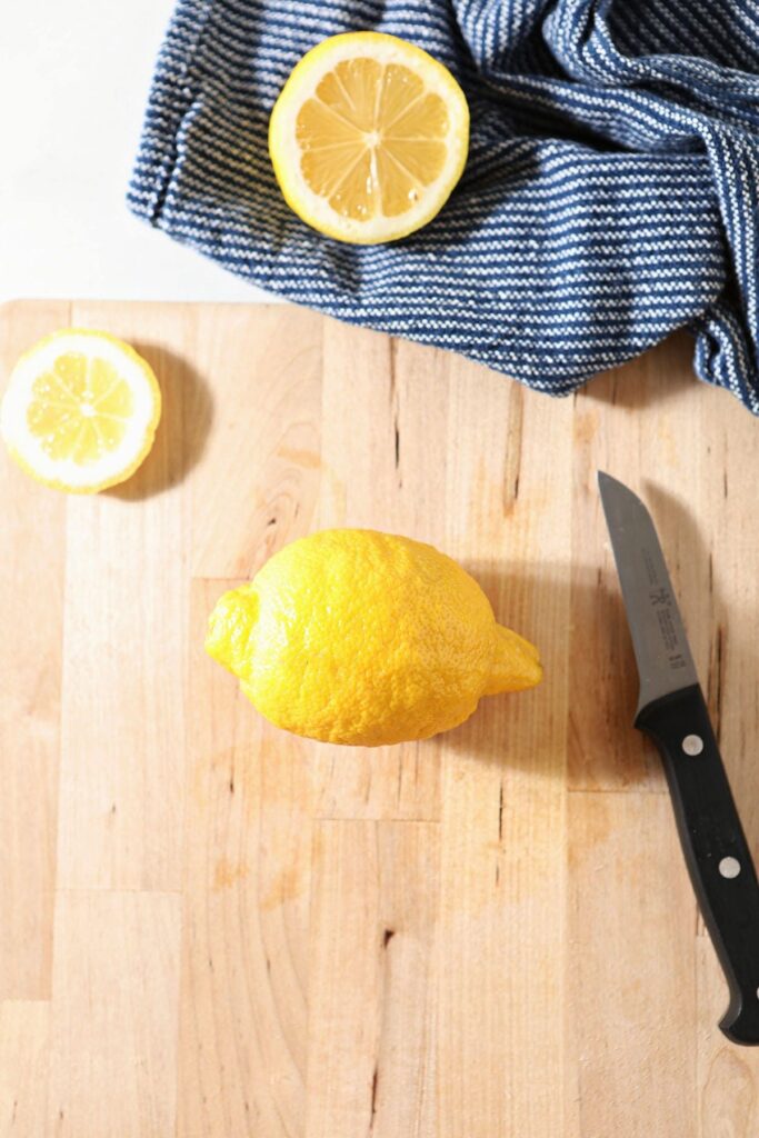 A lemon with a paring knife on a wooden cutting board