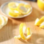 A lemon twist stands on a cutting board next to lemon slices