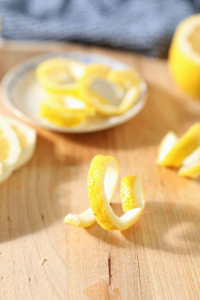 A lemon twist stands on a cutting board next to lemon slices