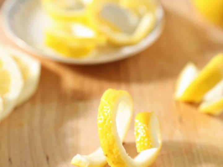 A lemon twist stands on a cutting board next to lemon slices