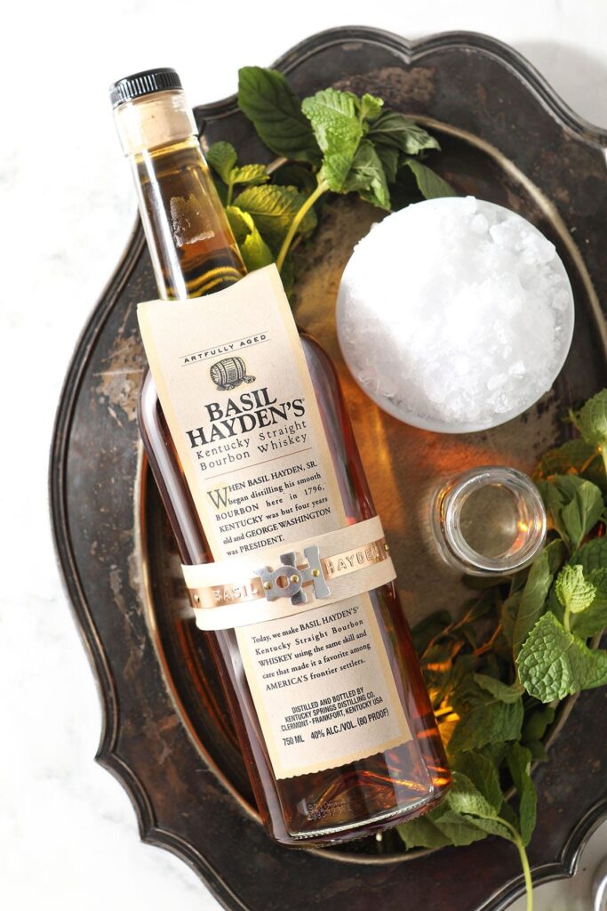 A bottle of Basil Hayden bourbon with crushed ice and other ingredients on a silver tray