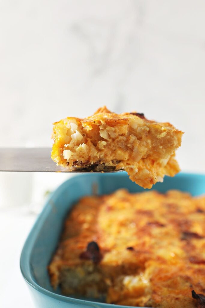 A spatula lifts a slice of tater tot egg casserole out of a dish