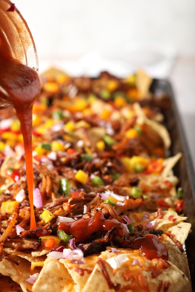 Barbecue sauce drizzles on top of pulled pork nachos