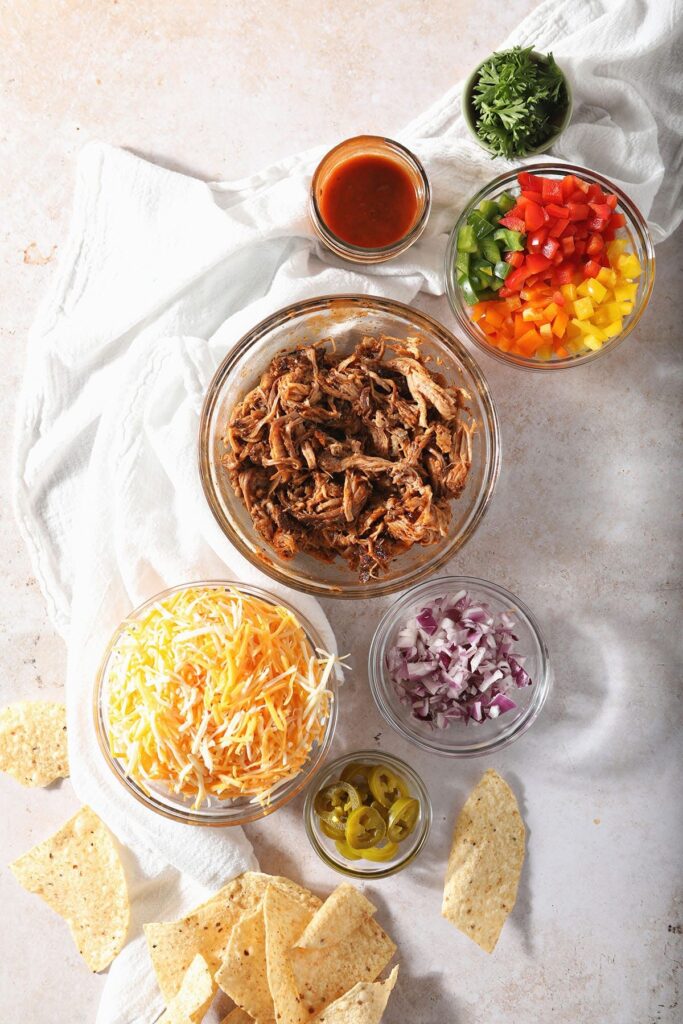 Bowls holding barbecue nacho ingredients in a white kitchen cloth