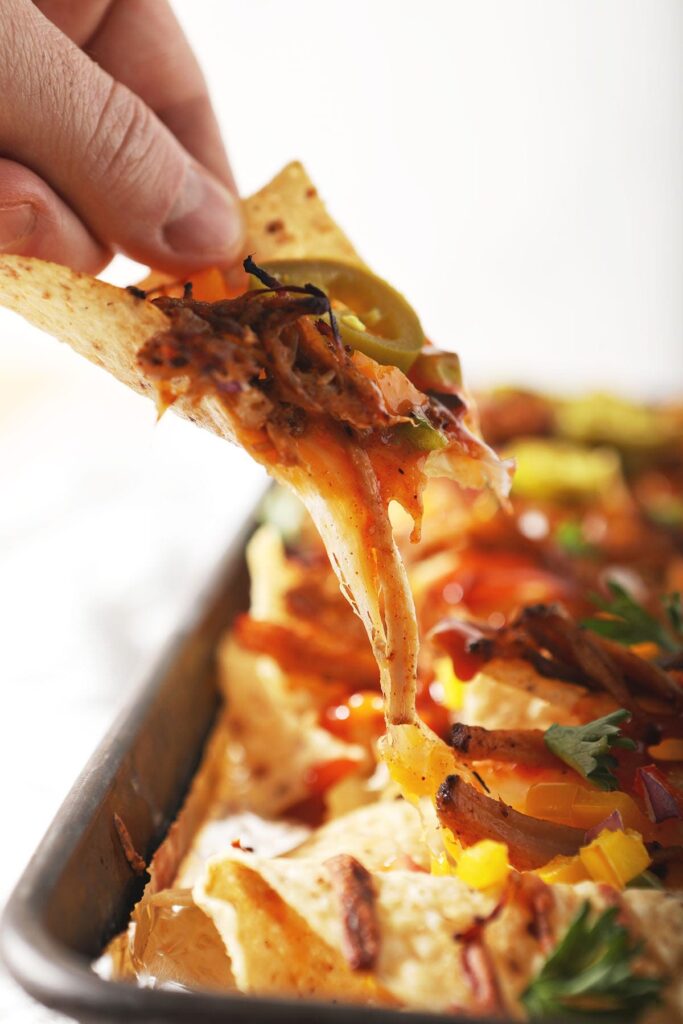 A person lifts a BBQ nacho from a pan