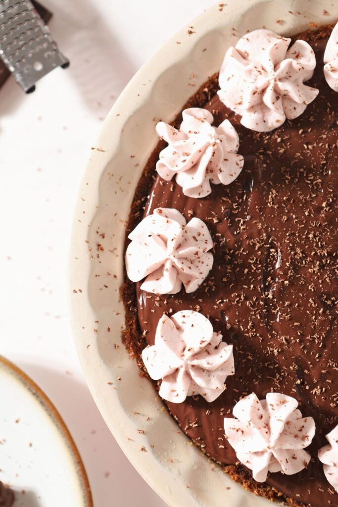 A chocolate pudding pie garnished with strawberry whipped cream and chocolate shavings