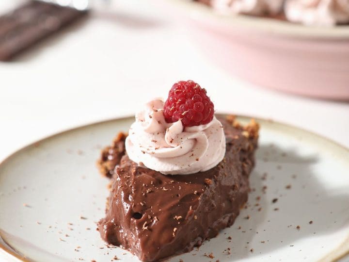 A slice of chocolate pudding pie with graham cracker pie crust on a plate