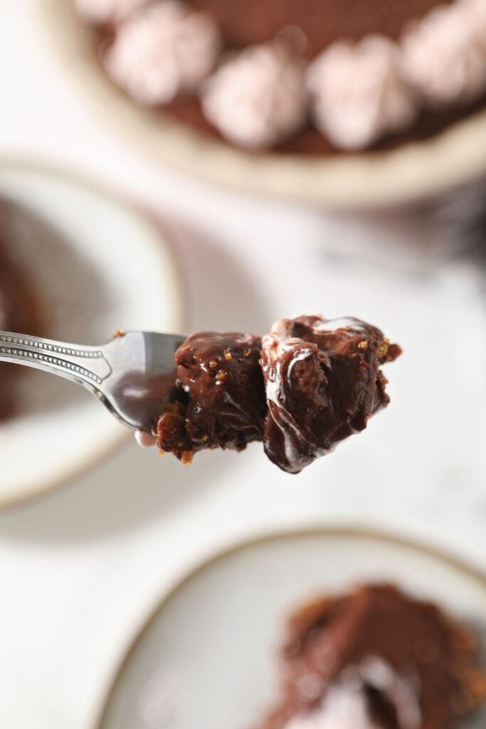 A fork holds a bite of chocolate pudding pie above plates