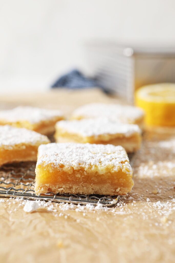 A lemon bar sits on a metal grate with other lemon bars