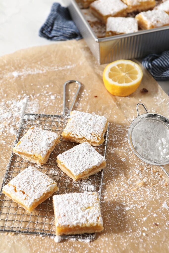  Five lemon bars sit on a metal cooling rack next to a tray of bars