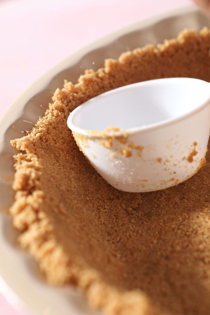 A white measuring scoop pushes graham cracker crumbs into place