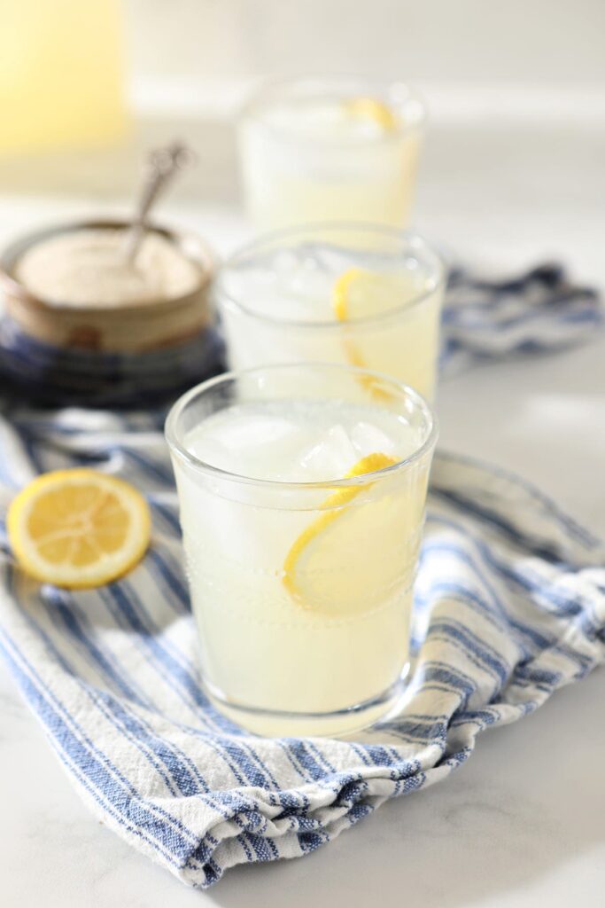 Three glasses of lemonade with lemon garnishes on a blue striped towel