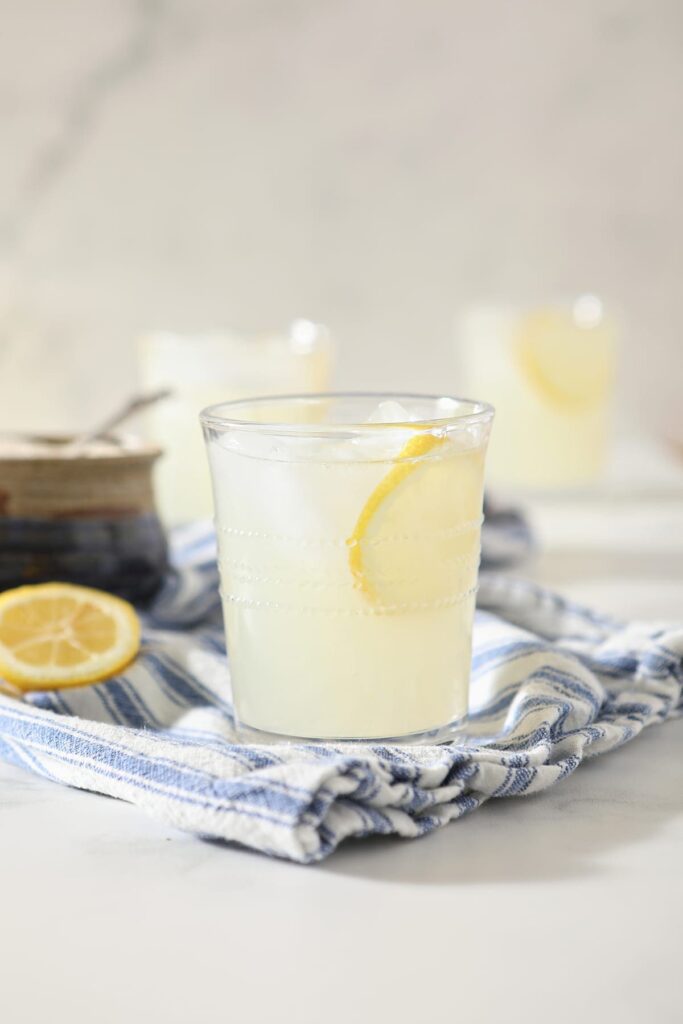  A glass of fresh squeezed lemonade garnished with a lemon round on a blue and white towel