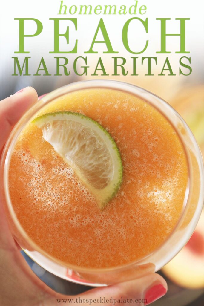 A hand holds a peach margarita garnished with a lime wedge with text homemade peach margaritas