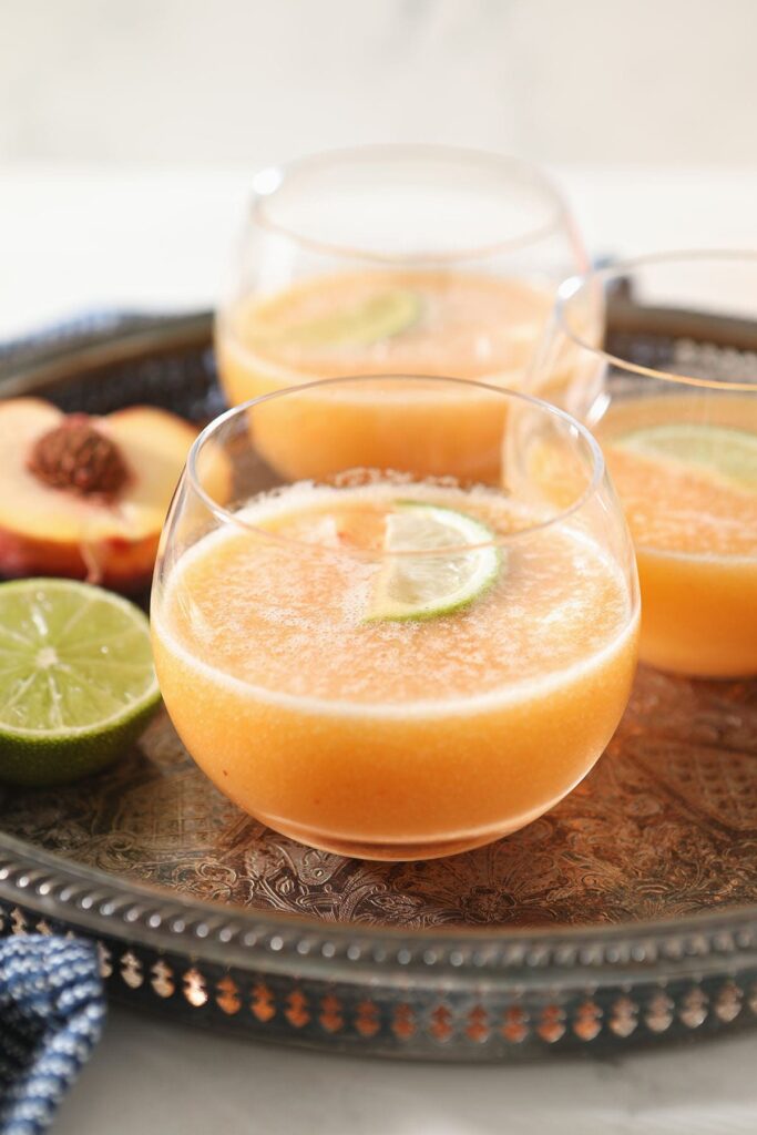 Three orange margaritas on a metal tray with limes