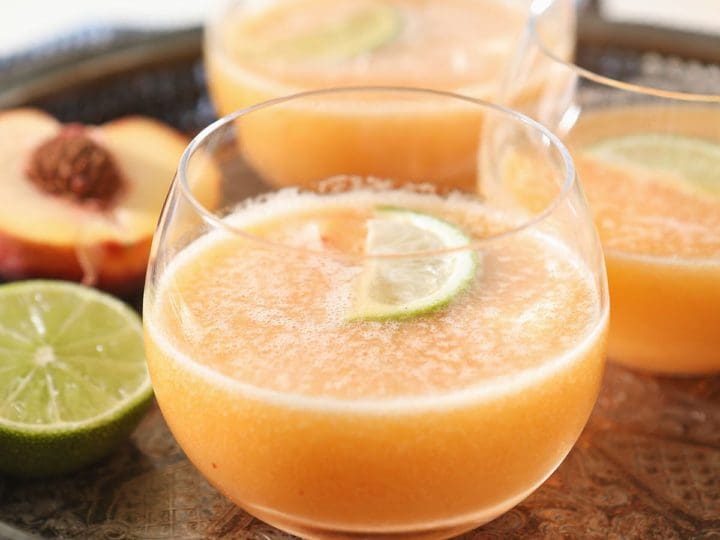Three orange margaritas on a metal tray with limes