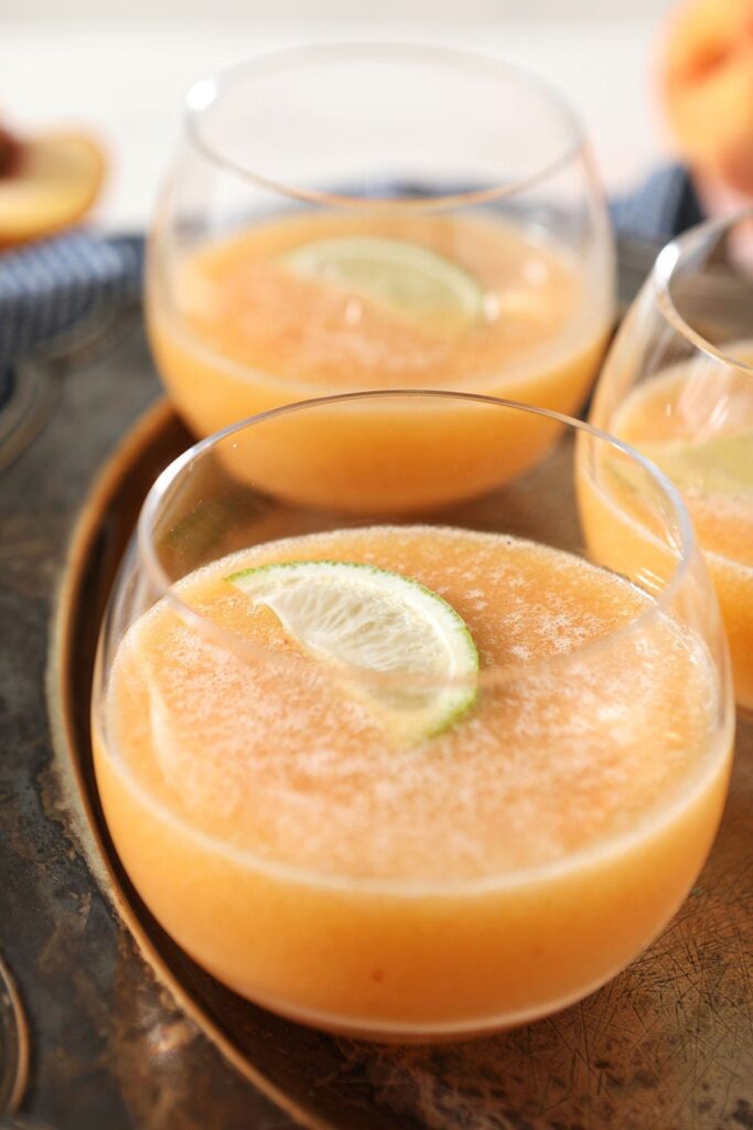 Three peach margaritas garnished with lime wedges on a metal tray