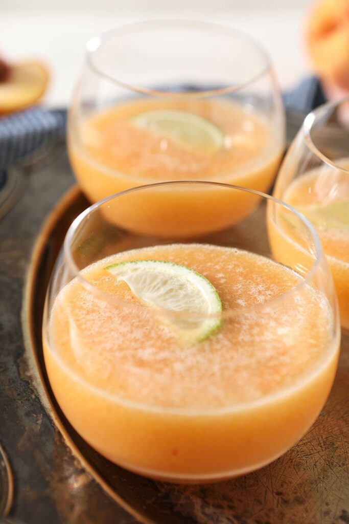  Three peach margaritas garnished with lime wedges on a metal tray