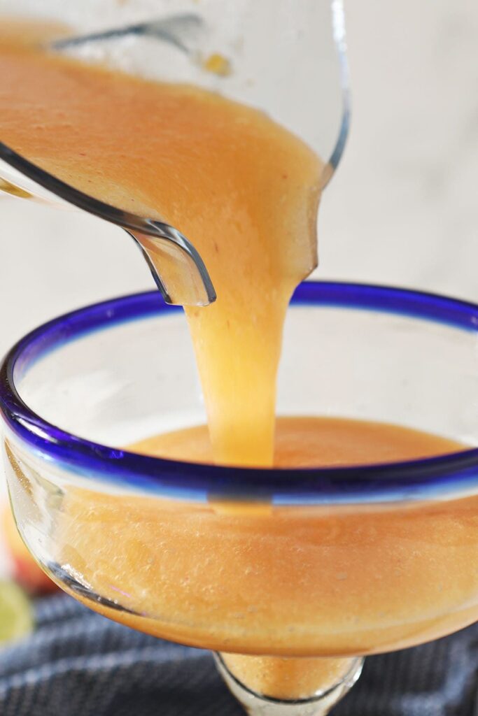 Peach margarita is poured from a blender into a margarita glass