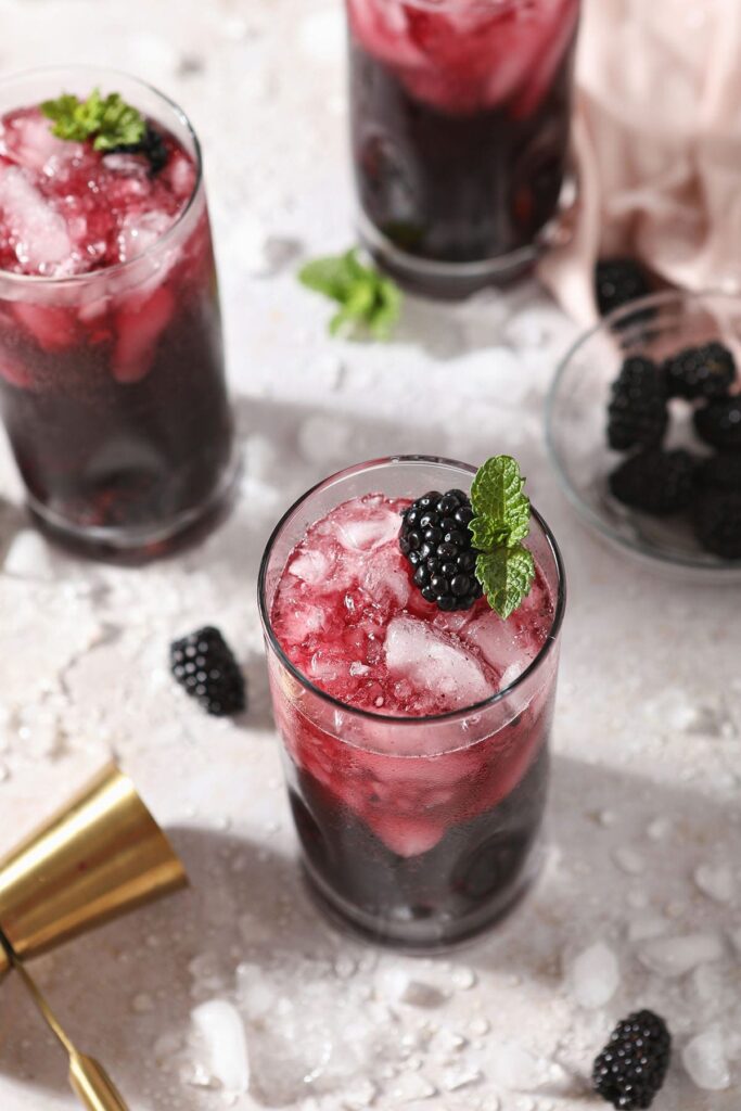 Three red wine spritzers garnished with blackberries and mint