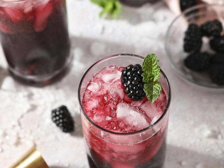 Three red wine spritzers garnished with blackberries and mint