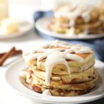 A stack of Cinnamon Roll Pancakes with glaze on a white plate