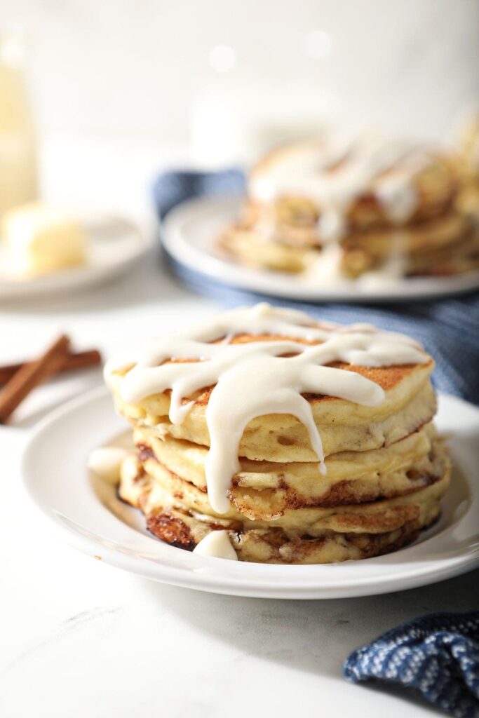 A stack of Cinnamon Roll Pancakes with glaze on a white plate