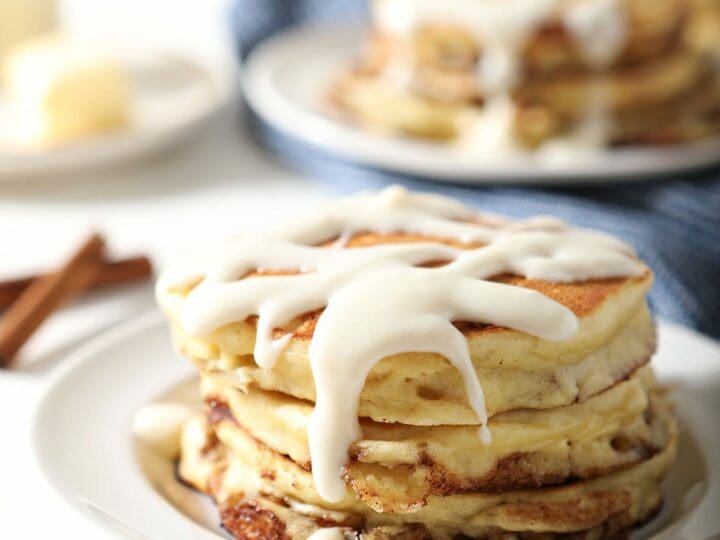 A stack of Cinnamon Roll Pancakes with glaze on a white plate