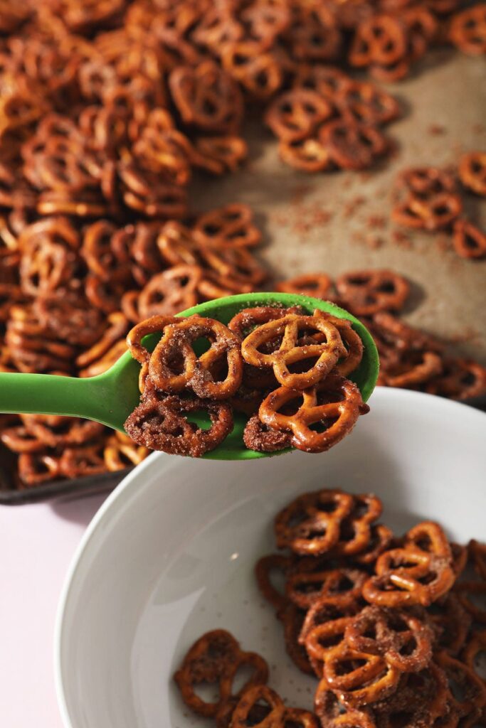 A green spoon transfers pretzels from a baking sheet to a bowl