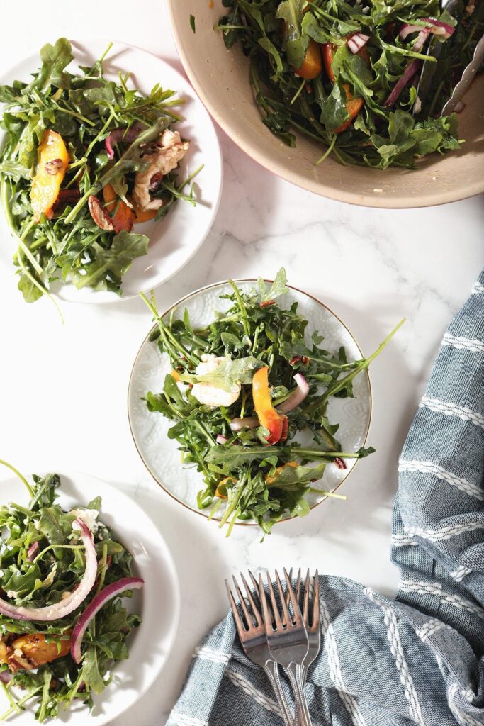 Three white plates hold grilled peach salad next to a salad bowl