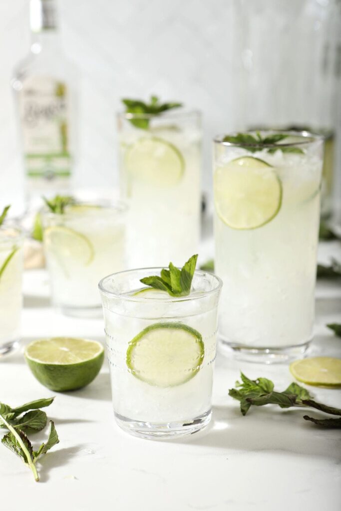 Five mojito glasses with a pitcher and a bottle of rum