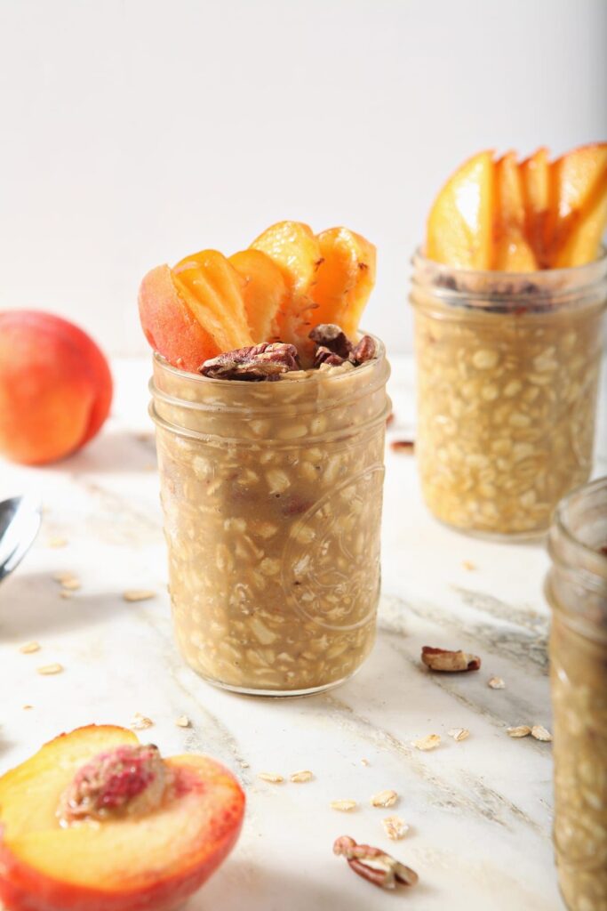 Three jars of Peach Overnight Oats with peach slices and toasted pecan garnishes