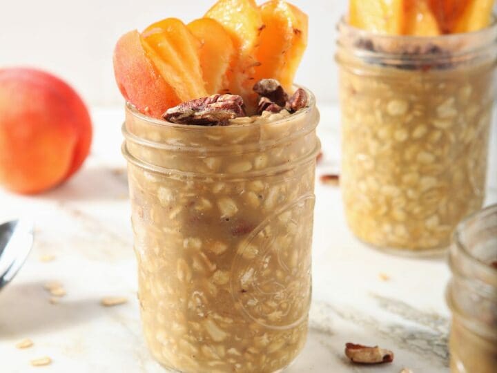 Three jars of Peach Overnight Oats with peach slices and toasted pecan garnishes