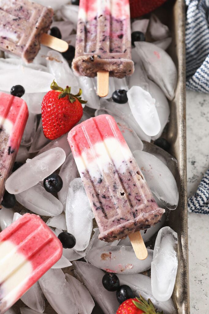 Five red white and blue popsicles on a tray of ice