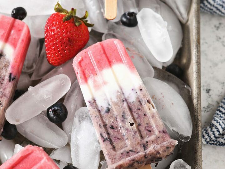Five red white and blue popsicles on a tray of ice