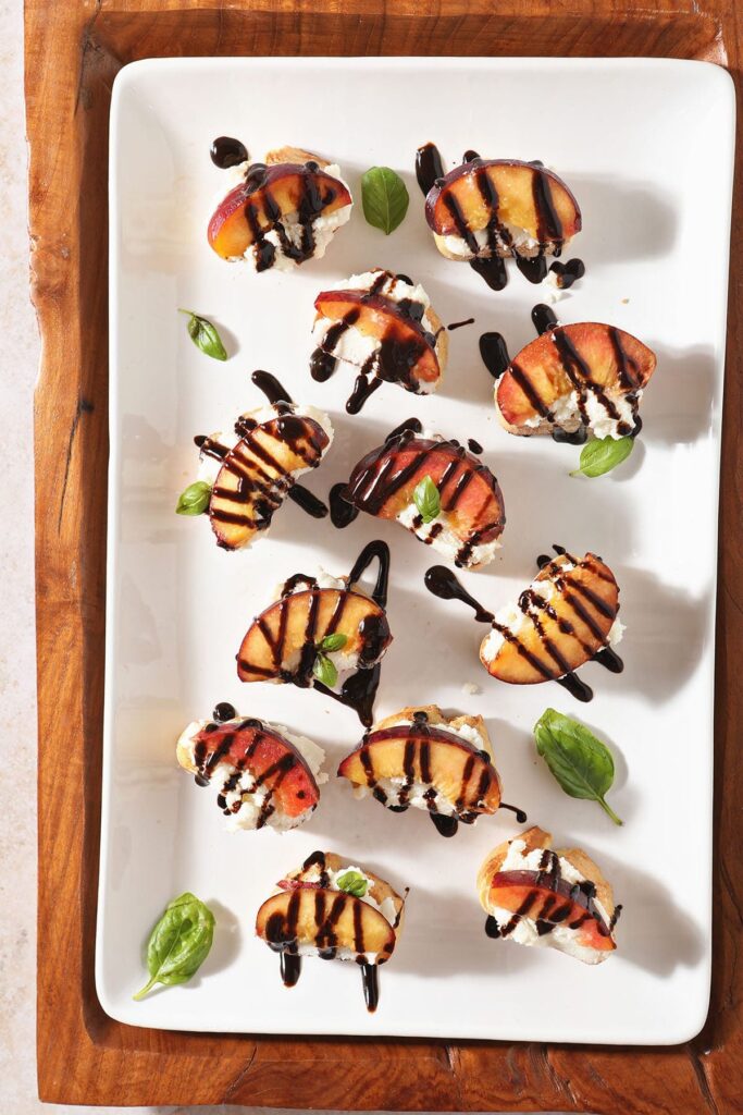 A white platter of several Ricotta Crostini with Grilled Peaches