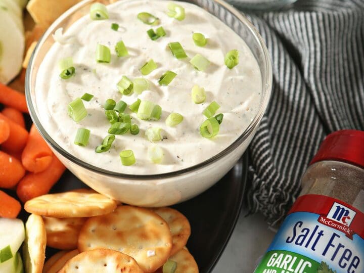 A bowl of Garlic and Herb Cream Cheese Dip with dippers and a jar of a McCormick spice blend