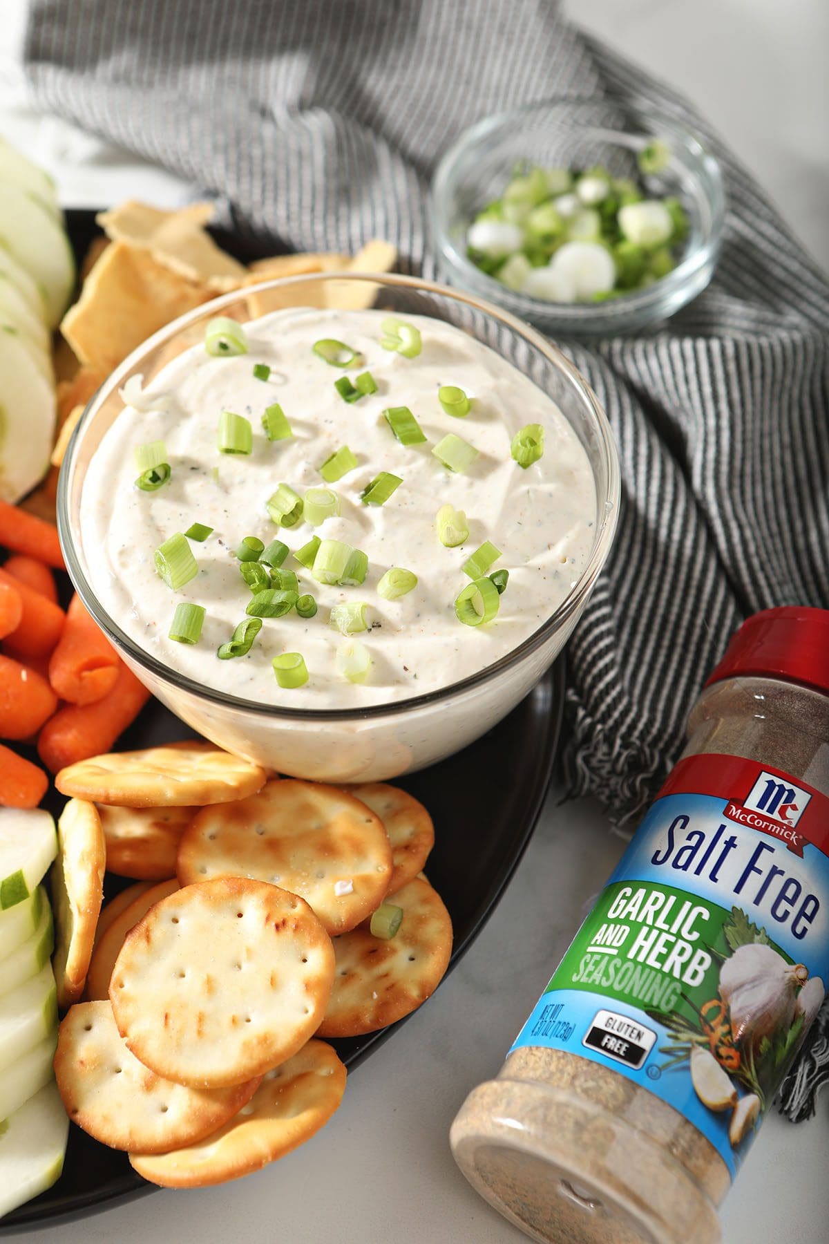 A bowl of Garlic and Herb Cream Cheese Dip with dippers and a jar of a McCormick spice blend