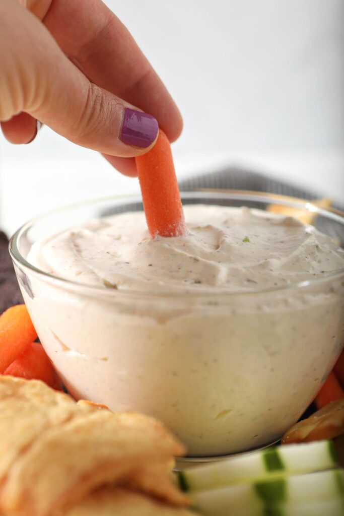 A carrot dips into a bowl of cream cheese dip