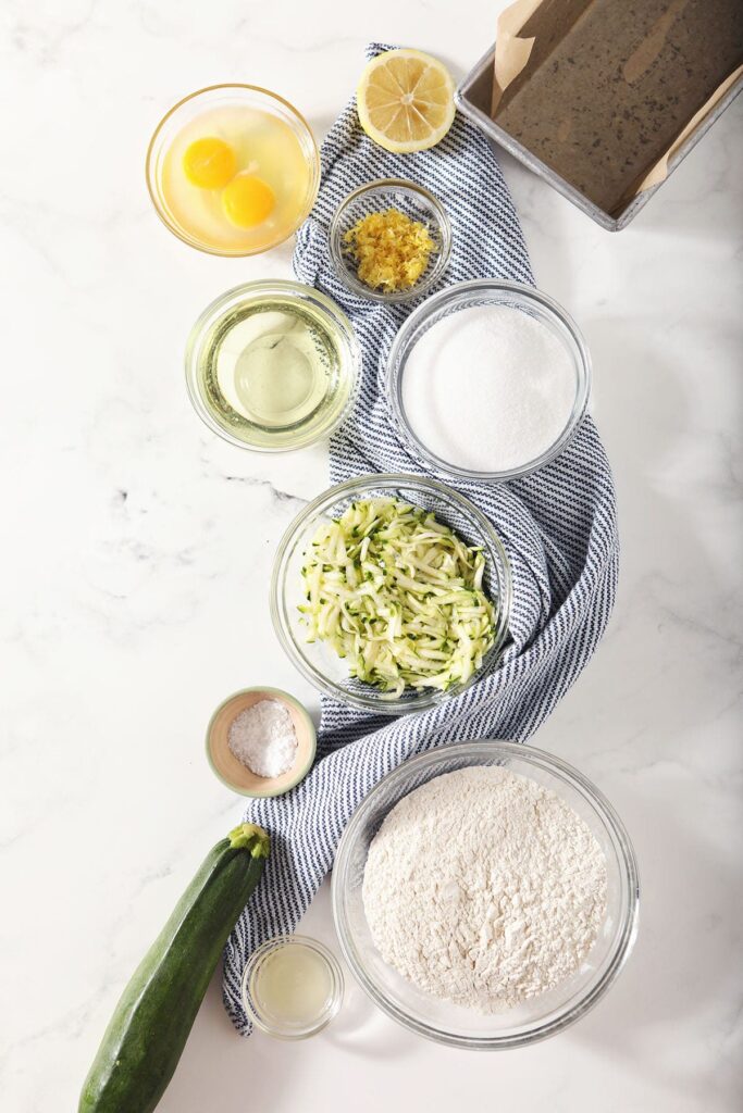 Ingredients for zucchini quick bread in bowls on marble