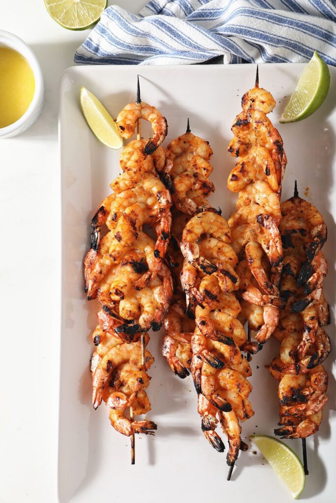 Skewered blackened shrimp with lime wedges on a white plate