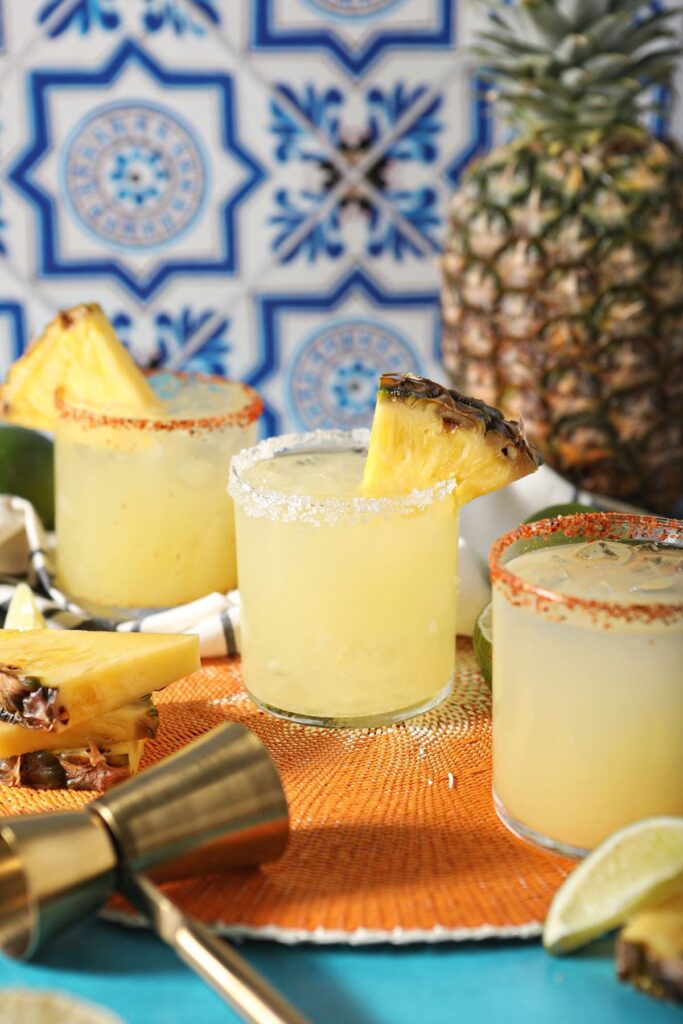 Three pineapple cocktails on an orange woven placemat