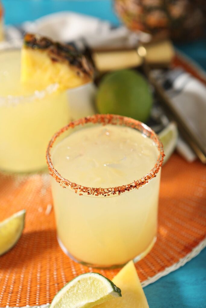 A tajin-rimmed pineapple margarita on an orange placemat