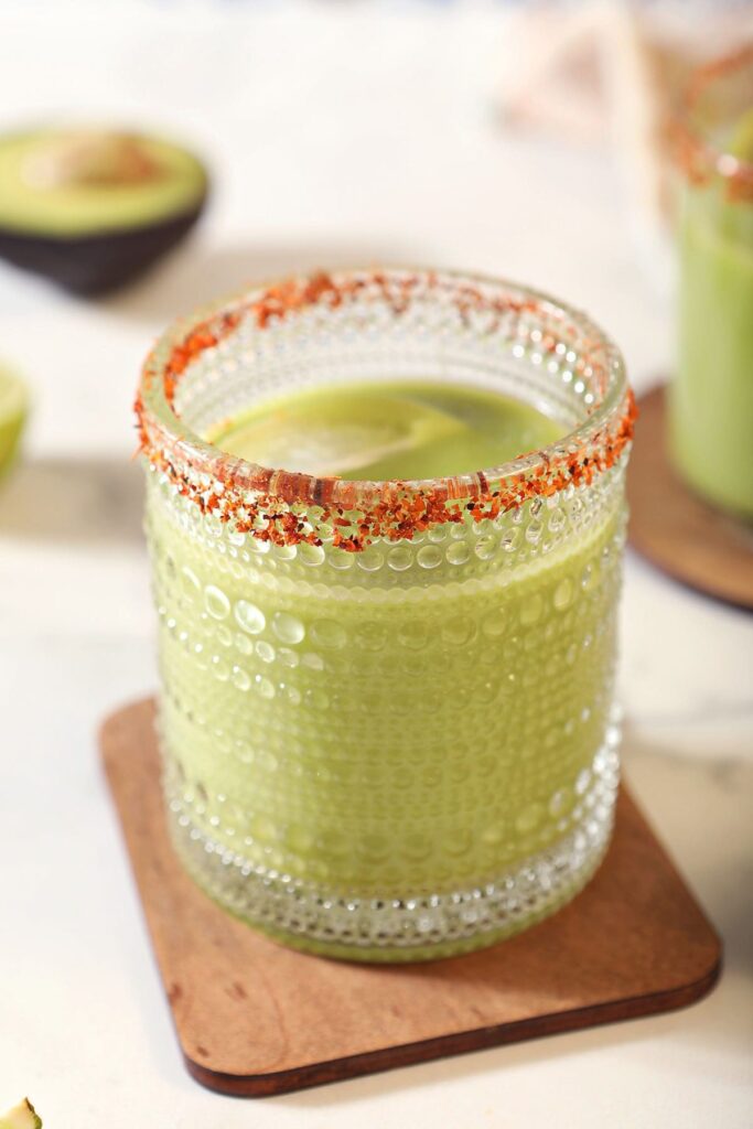 An Avocado Margarita on a wooden coaster with a tajin rim