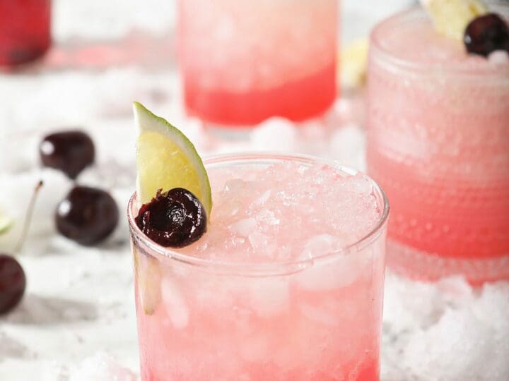 Three cherry limeades surrounded by ice and cherries