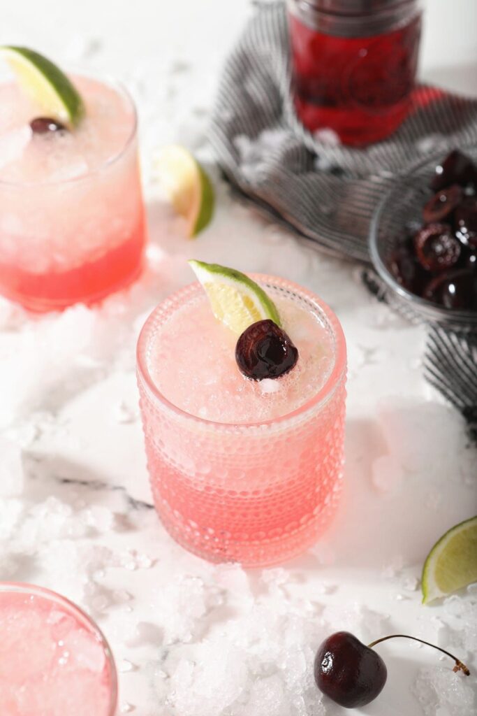 A cherry limeade on marble with a cherry and lime garnish