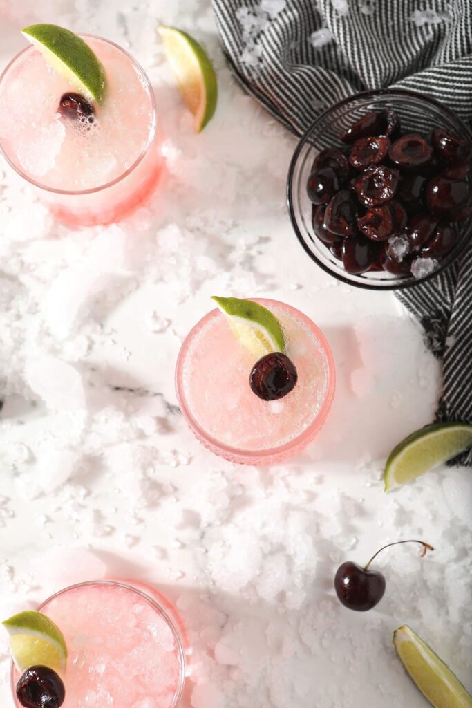 Three limeades with cherries and limes with ice and a bowl of cherries