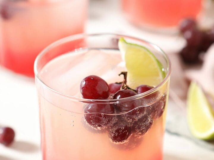 A cocktail with fresh grapes and a lime floating in it on marble