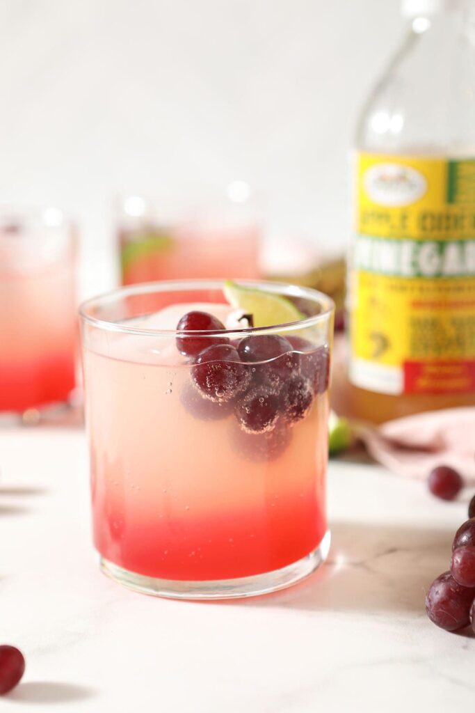 A pink mocktail garnished with fresh grapes and a lime wedge