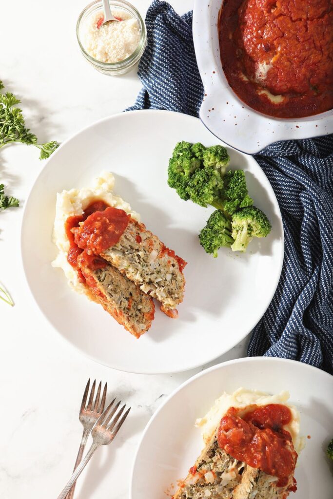 Slices of meatloaf with mashed potatoes and broccoli on white plates